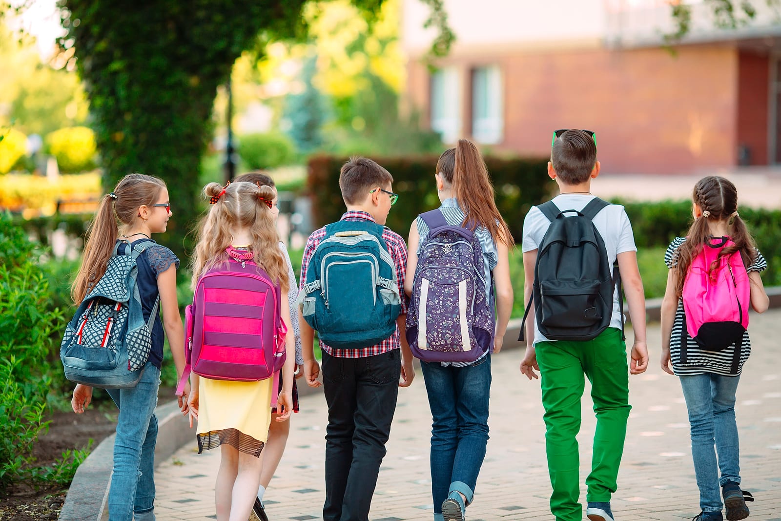 Children seen from behind walking outdoors wearing backpacks